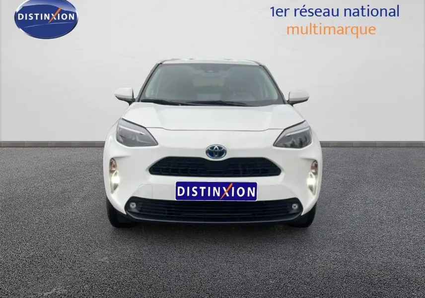 Vue frontale d'une Toyota Yaris Cross Hybrid blanche 2024 avec phares allumés sur fond neutre.