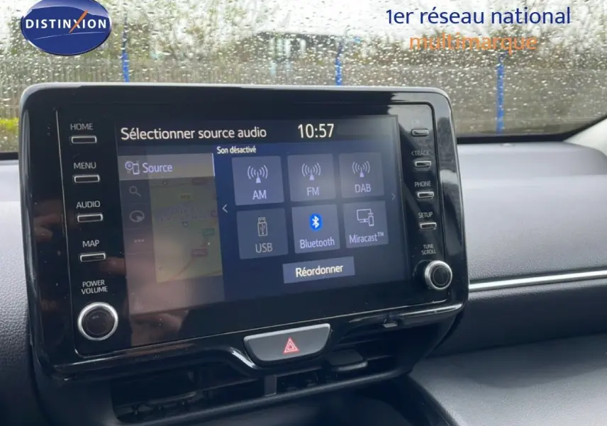 Vue intérieure centrée sur l'écran tactile multimédia de la Toyota Yaris Cross Hybrid blanche, avec commandes visibles.