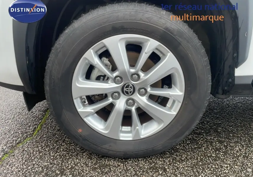 Gros plan sur la roue avant droite avec jante alliage argentée du Toyota Yaris Cross blanc hybride 2024.