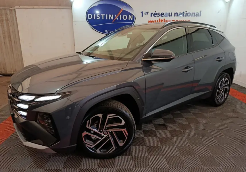 Vue 3/4 avant droit du Hyundai Tucson 1.6 Hybrid gris foncé avec jantes au design géométrique et feux LED allumés.