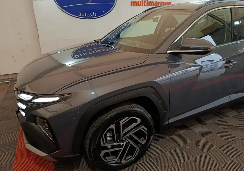 Vue 3/4 avant droit d'un Hyundai Tucson gris foncé avec jantes alliage au design moderne et phares LED allumés.