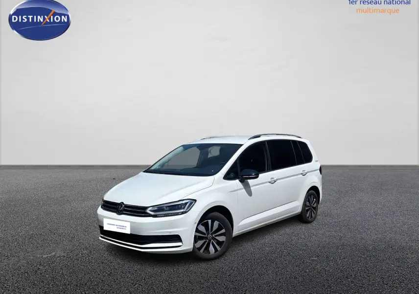 Volkswagen Touran blanc vue 3/4 avant droit, avec jantes alliage et vitres arrière surteintées.
