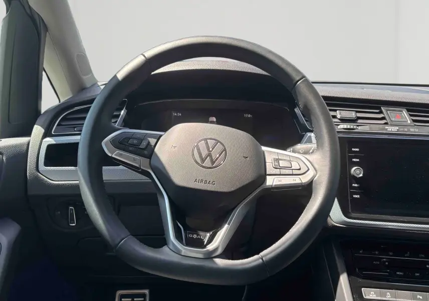 Vue intérieure centrée sur le volant cuir multifonctions du Volkswagen Touran blanc, avec tableau de bord et écran tactile visible.