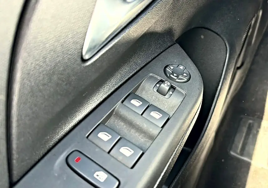 Gros plan sur les commandes de lève-vitres et rétroviseurs électriques côté conducteur de l’Opel Corsa noire.