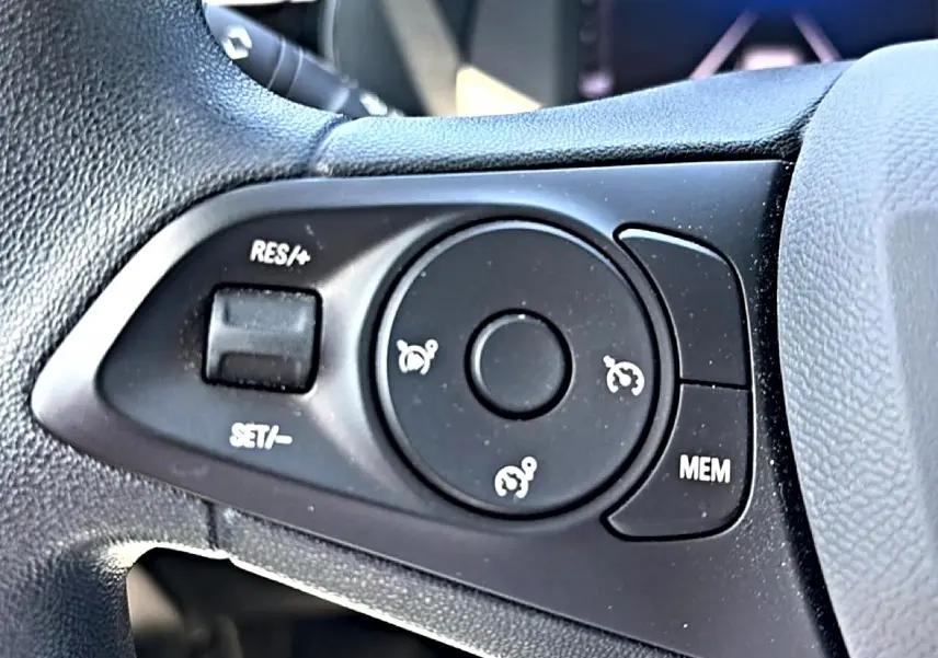 Gros plan sur les commandes de régulateur de vitesse au volant noir de l’Opel Corsa 1.2 turbo 100 édition.