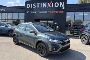 Vue 3/4 avant droite d'une Dacia Sandero III Stepway Vert Cèdre avec jantes noires et rétroviseurs cuivrés, devant un showroom Distinxion.