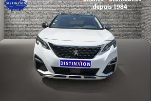 Vue avant d'un Peugeot 3008 blanc nacré avec calandre noire et logo lion au centre, sur fond de mur en briques grises.