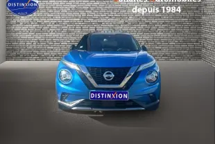Vue avant d'un Nissan Juke 2020 bleu clair avec calandre chromée et phares allumés sur fond de mur en briques.