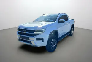 Volkswagen Amarok V6 blanc en 3/4 avant droit avec jantes alu 21 pouces et barres de toit visibles.