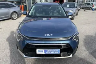 Vue frontale d’un KIA Niro bleu métal 2024 avec calandre noire et logo KIA moderne, en extérieur sur parking.
