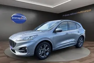 Vue 3/4 avant droite d'un Ford Kuga gris 2024 hybride essence, finition ST-LINE X avec jantes foncées et calandre distinctive.