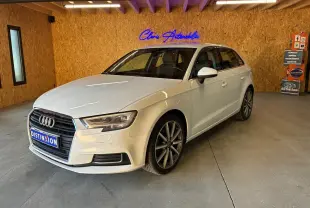 Audi A3 Sportback blanc vue 3/4 avant droit dans un intérieur avec mur en bois et enseigne lumineuse bleue.
