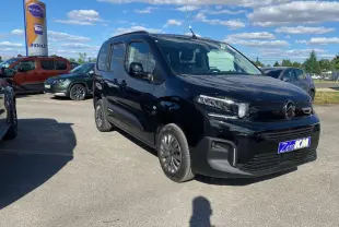 Vue 3/4 avant droit d'un Citroën Berlingo noir métallisé garé en extérieur sous un ciel bleu avec quelques nuages.