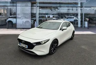 Vue 3/4 avant d'une Mazda3 blanche 2020 avec jantes noires, stationnée devant une concession Mazda.