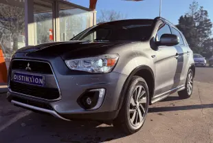 Vue 3/4 avant droit d’un Mitsubishi ASX gris métallisé garé sous un abri avec jantes alliage et calandre noire.