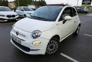 Fiat 500 Cabriolet blanche vue en 3/4 avant droit, toit ouvert partiellement, phare avant droit allumé sur parking.