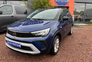 Opel Crossland bleu clair en 3/4 avant droit avec toit noir, stationné devant un bâtiment commercial.