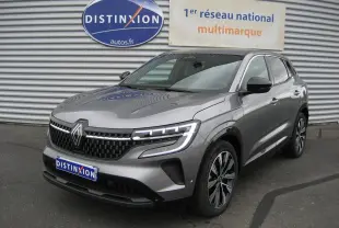 Renault Austral gris 3/4 avant droit, phares LED allumés, calandre noire et jantes bi-ton 19 pouces visibles.