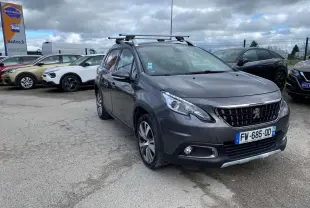 Peugeot 2008 gris platinium vue 3/4 avant droit avec barres de toit aluminium sur parking extérieur.