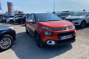 Citroën C3 orange vue 3/4 avant droit sur parking, avec toit noir et protections latérales noires.
