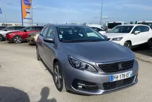Peugeot 308 SW gris Artense métal vue 3/4 avant droit sur parking avec calandre noire et phares LED.