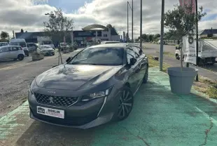 Peugeot 508 SW gris vue 3/4 avant droit, stationnée en extérieur avec calandre distinctive et jantes noires.