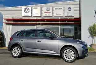 Vue de profil côté gauche d'un Skoda Kamiq gris graphite métal 2024 garé devant un service automobile.