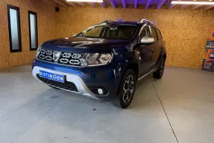 Vue 3/4 avant d'un Dacia Duster bleu avec calandre chromée et jantes alliage 17 pouces dans un garage.