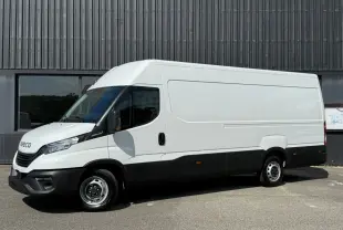 Vue de profil côté gauche d’un utilitaire Iveco Daily blanc avec bas de caisse noir, stationné devant un bâtiment industriel.