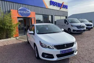 Peugeot 308 blanc nacré vue 3/4 avant droit devant un concessionnaire Distinxion par temps clair.