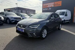 SEAT Ibiza 1.0 EcoTSI 95 Xcellence gris Magnetic Tech vue 3/4 avant sur parking avec panneau promotionnel en arrière-plan
