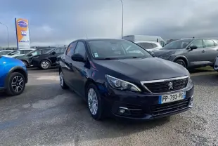 Peugeot 308 bleu foncé vue 3/4 avant droit sur parking avec calandre chromée et feux LED allumés.