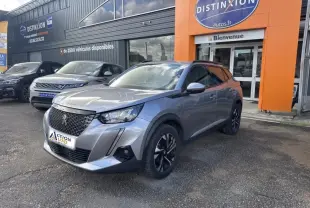 Peugeot 2008 gris Artense vue 3/4 avant droit, avec jantes alliage et calandre noire, stationnée devant un concessionnaire.