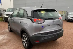 Vue 3/4 arrière droite d'un Opel Crossland gris métallisé avec feux arrière allumés sur parking humide.