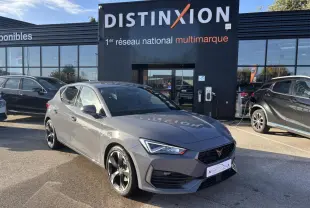 Vue 3/4 avant d'une CUPRA Leon gris Graphene avec jantes alliage noires devant un showroom Distinxion.