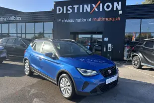 Vue 3/4 avant d'un SEAT Arona bleu saphir avec toit noir, stationné devant un bâtiment Distinxion.