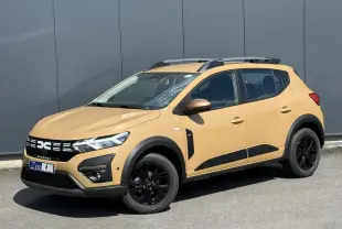 Vue 3/4 avant droite d'une Dacia Sandero Stepway beige Safari avec jantes noires et barres de toit grises.
