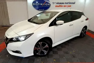 Nissan Leaf blanche vue en 3/4 avant droit dans un showroom avec logo Distinxion en arrière-plan.