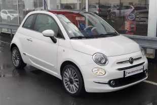 Fiat 500 Lounge blanche Bossa Nova vue 3/4 avant droit, phares allumés et jantes alliage multibranches.