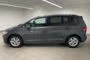 Profil droit d'un Volkswagen Touran 2024 gris dauphin, monospace diesel 7 places avec jantes alliage et toit équipé de barres longitudinales.