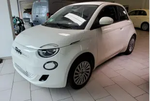 Vue 3/4 avant droite d'une Fiat 500 électrique blanche stationnée en intérieur avec jantes spécifiques et phares ronds LED.