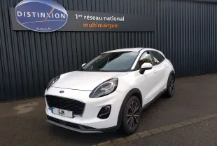 Ford Puma blanc en 3/4 avant droit, avec calandre noire et jantes foncées, stationné devant un mur gris.