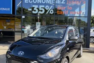 Vue 3/4 avant droite d'une Hyundai i10 noire 2025 garée devant un concessionnaire Distinxion avec logo visible.