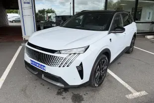 Peugeot 5008 HYBRID 145 e-DCS6 GT blanc Okenite avec toit noir, vue 3/4 avant droit sur parking devant vitrine.