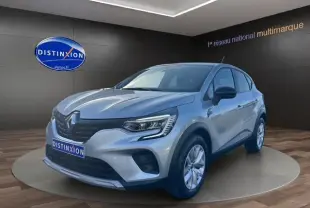 Renault Captur TCE 90 Evolution gris Highland en 3/4 avant droit, intérieur showroom avec logo Distinxion visible.