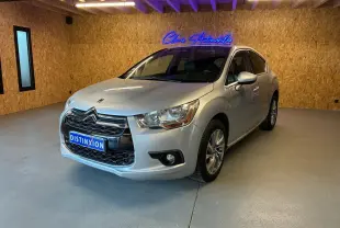 Vue 3/4 avant d'une DS4 gris clair, avec calandre chromée et jantes alliage dans un showroom au mur bois.