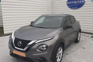 Nissan Juke gris 3/4 avant droit sous la pluie, avec calandre noire et phares ronds distinctifs.
