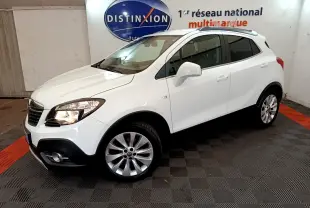 Opel Mokka blanc vue 3/4 avant droit en intérieur, avec jantes alliage et phares allumés.