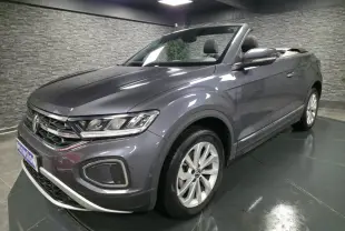Volkswagen T-Roc Cabriolet gris métallisé en 3/4 avant droit, capote noire ouverte et jantes alliage visibles.