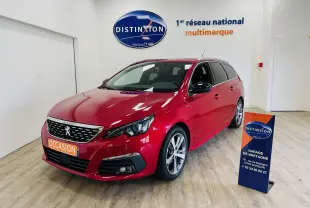 Peugeot 308 SW rouge vue 3/4 avant droit en intérieur, avec jantes alliage et plaque "OCCASION" visible.